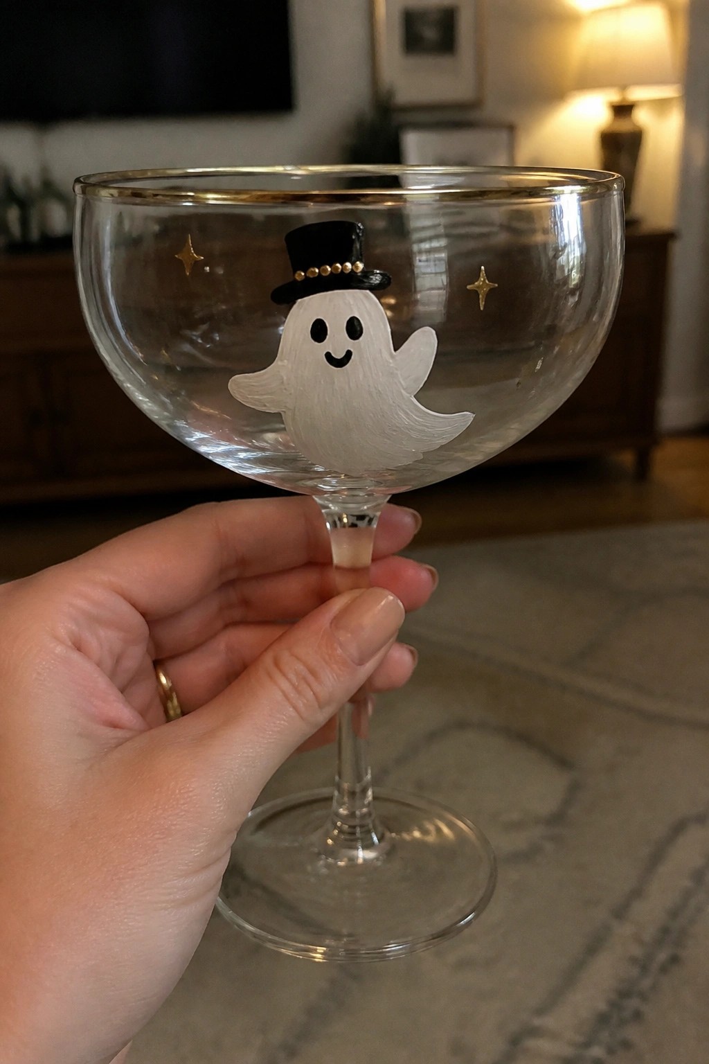 Hand holding coupe glass with white ghost, black top hat, and gold stars