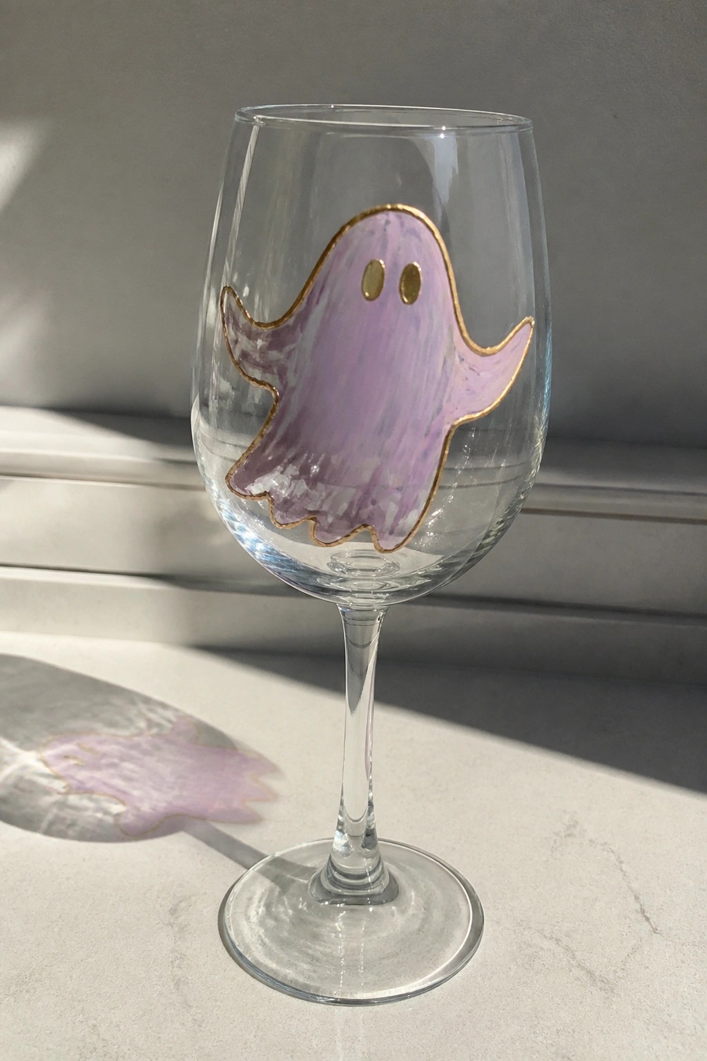 Clear wine glass with purple ghost outlined in gold on white surface