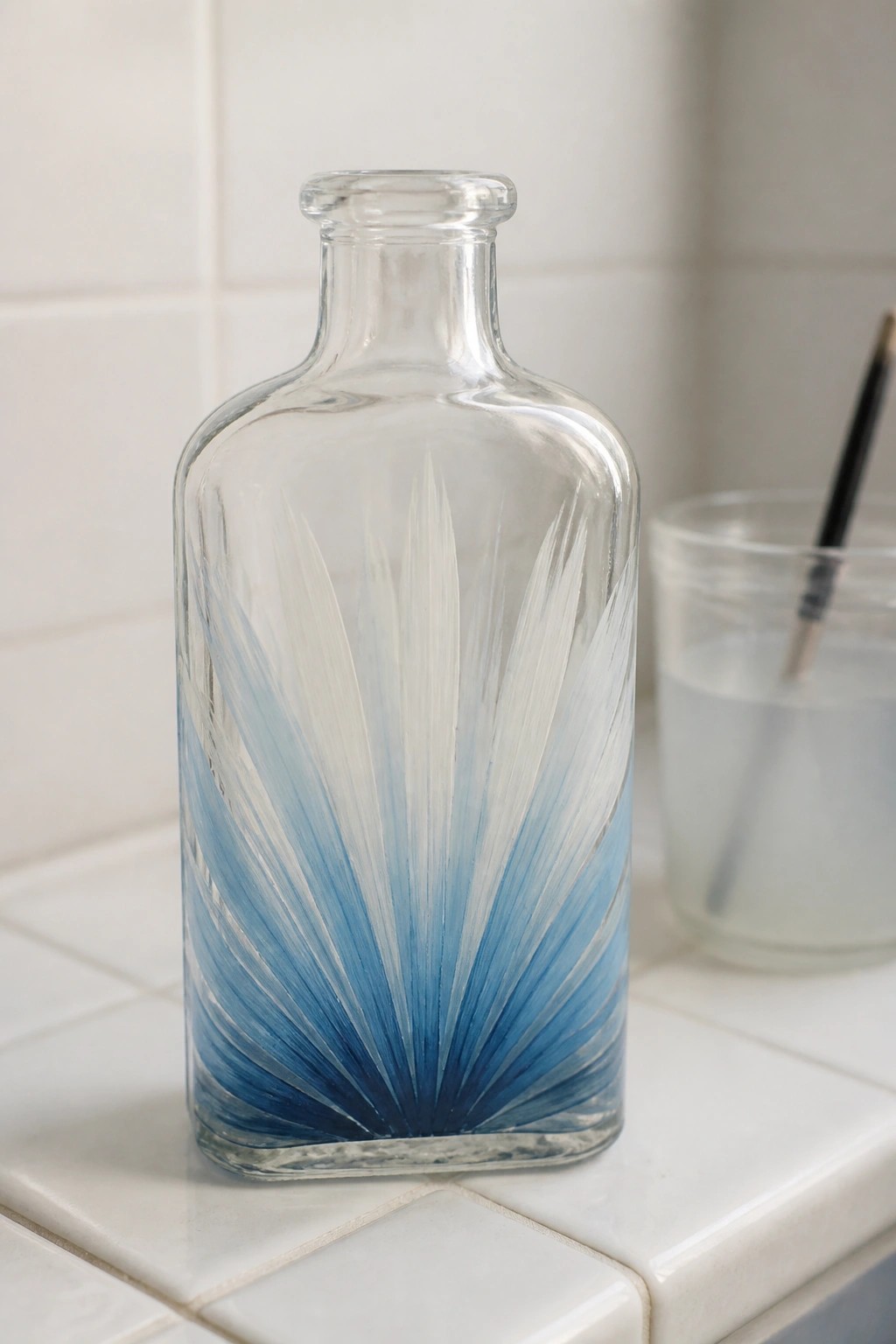 Clear glass bottle with blue gradient fan pattern on white tiled surface