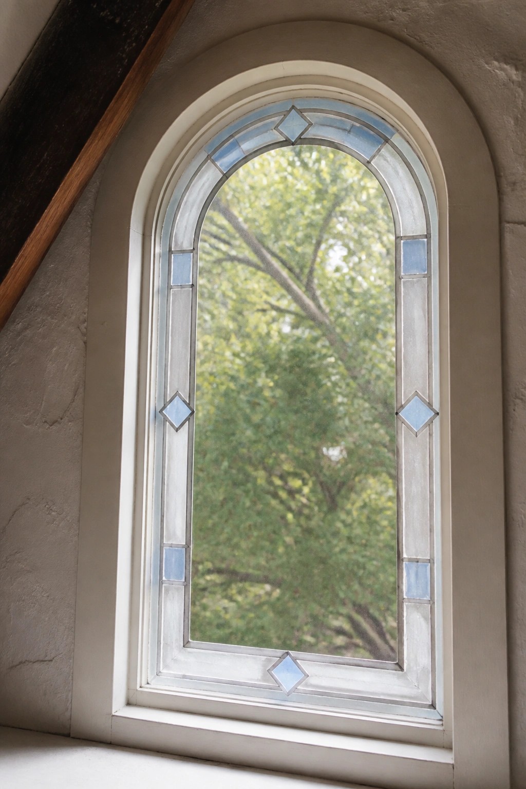 Arched window with blue diamond glass panes overlooking lush green trees