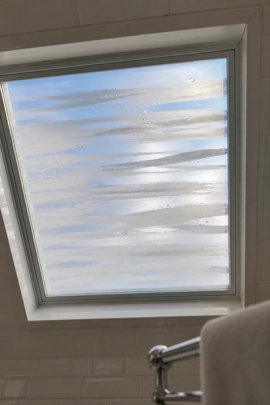 Frosted striped skylight showing blue sky above white tiles and chrome towel rack