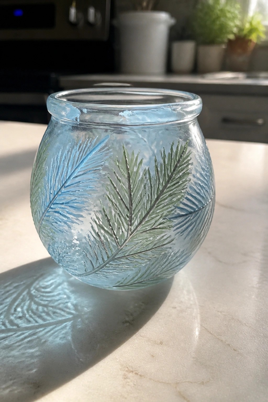Small blue glass bowl with etched pine branches on sunlit marble countertop