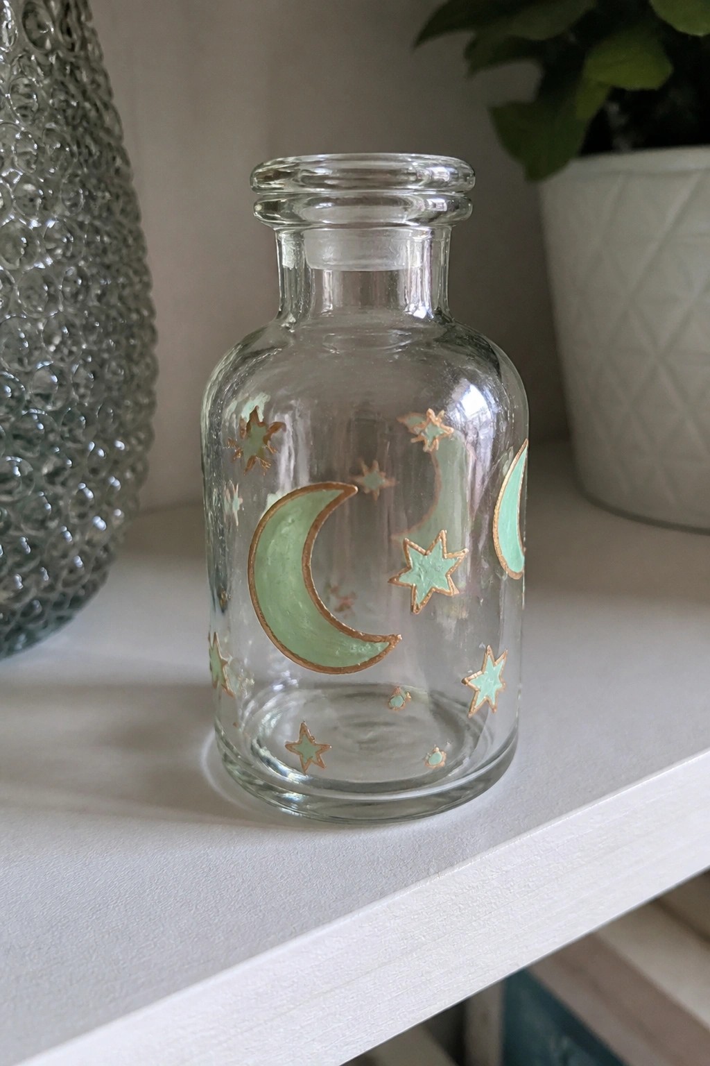 Clear glass bottle with mint green crescent moons and gold stars on shelf