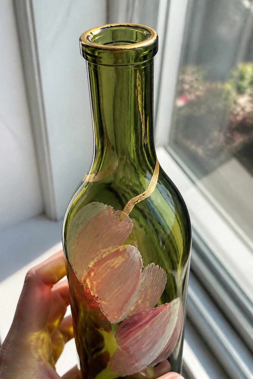 Hand holding green glass bottle with pink flowers and gold accents