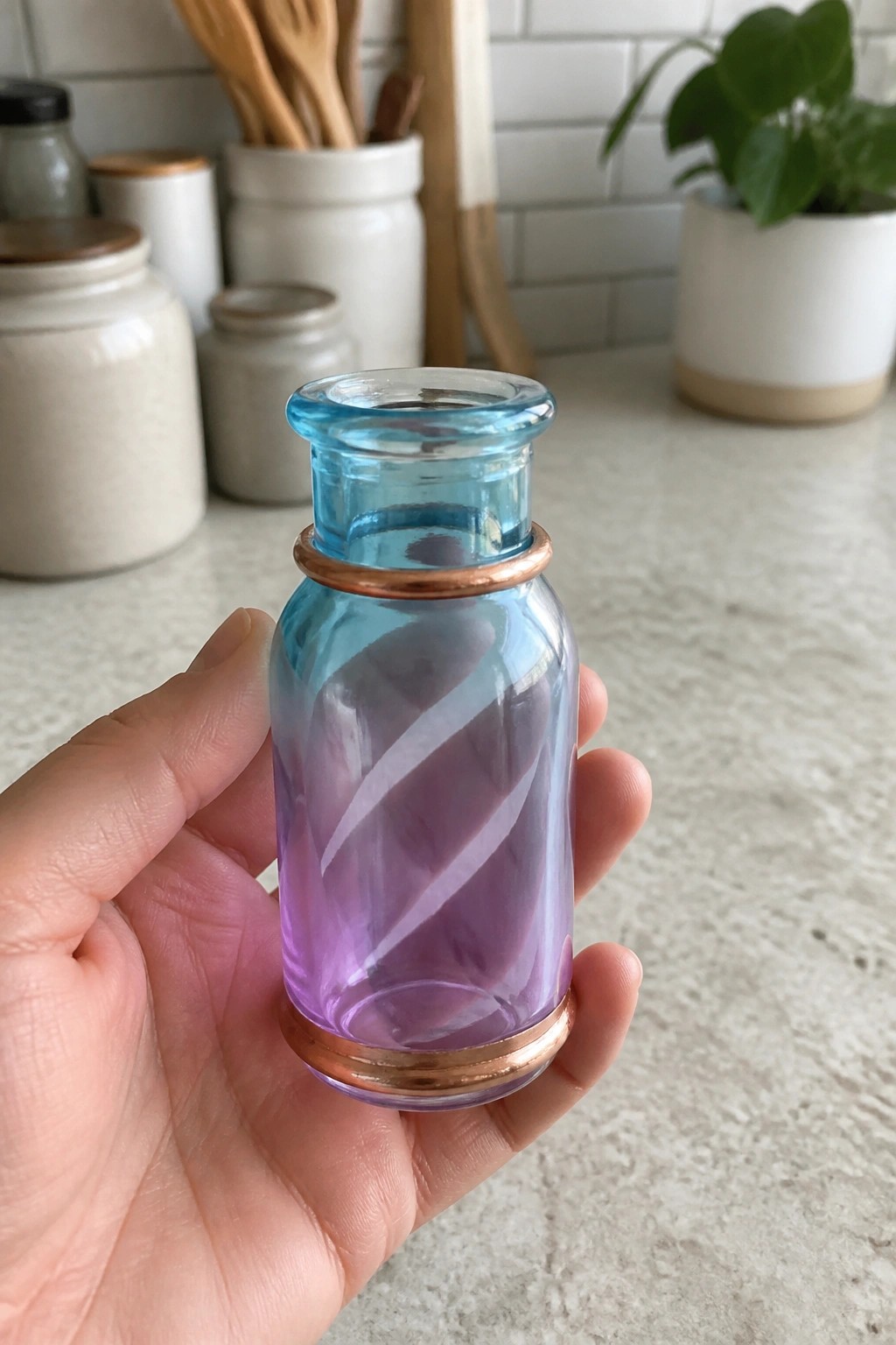 Hand holding small blue-purple glass bottle with white swirls and copper bands