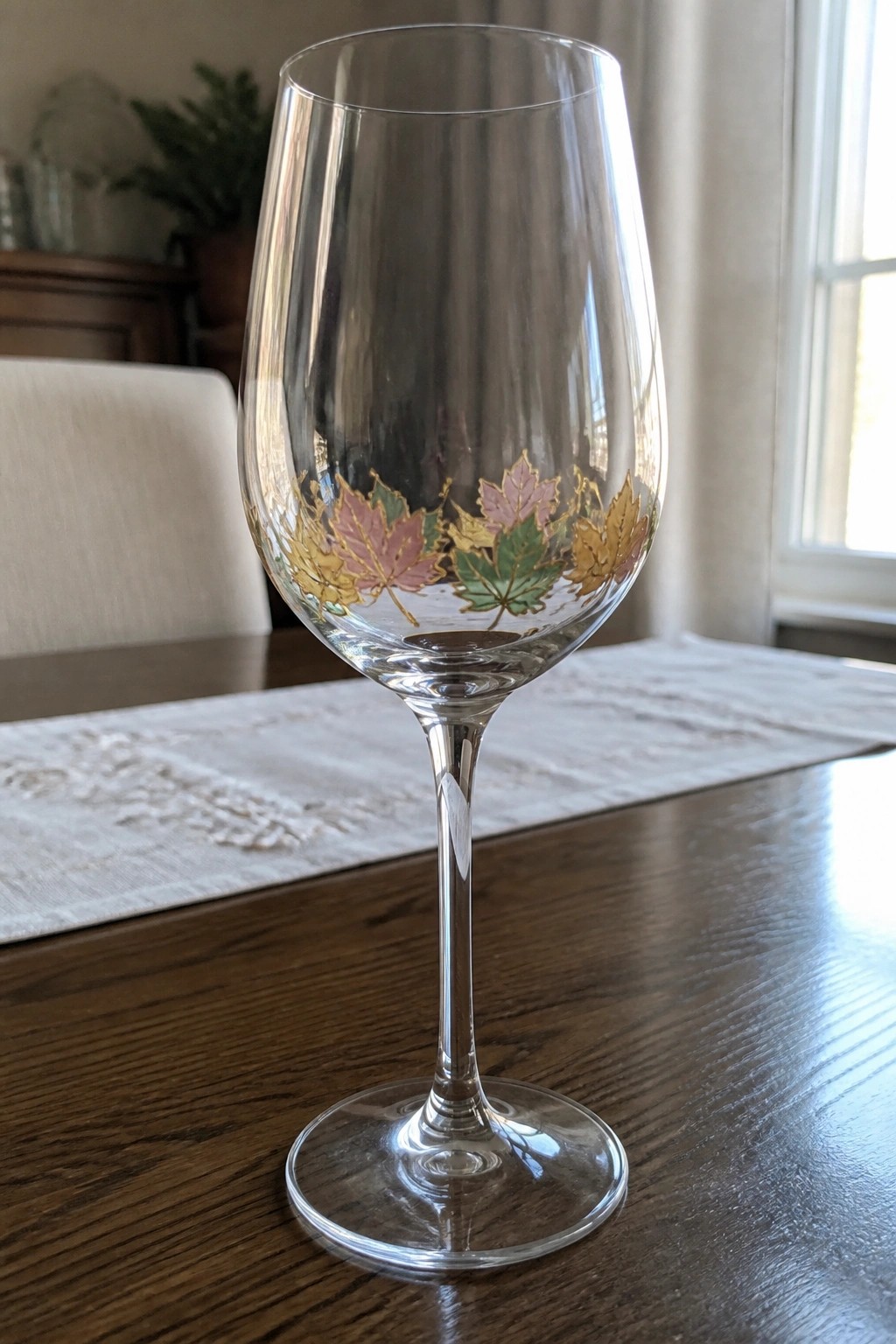 Clear wine glass with pink, yellow, green, and gold maple leaves on wood table