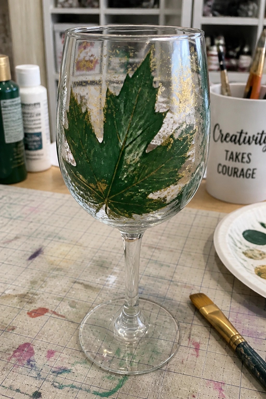 Wine glass with green maple leaf and gold accents on gridded mat