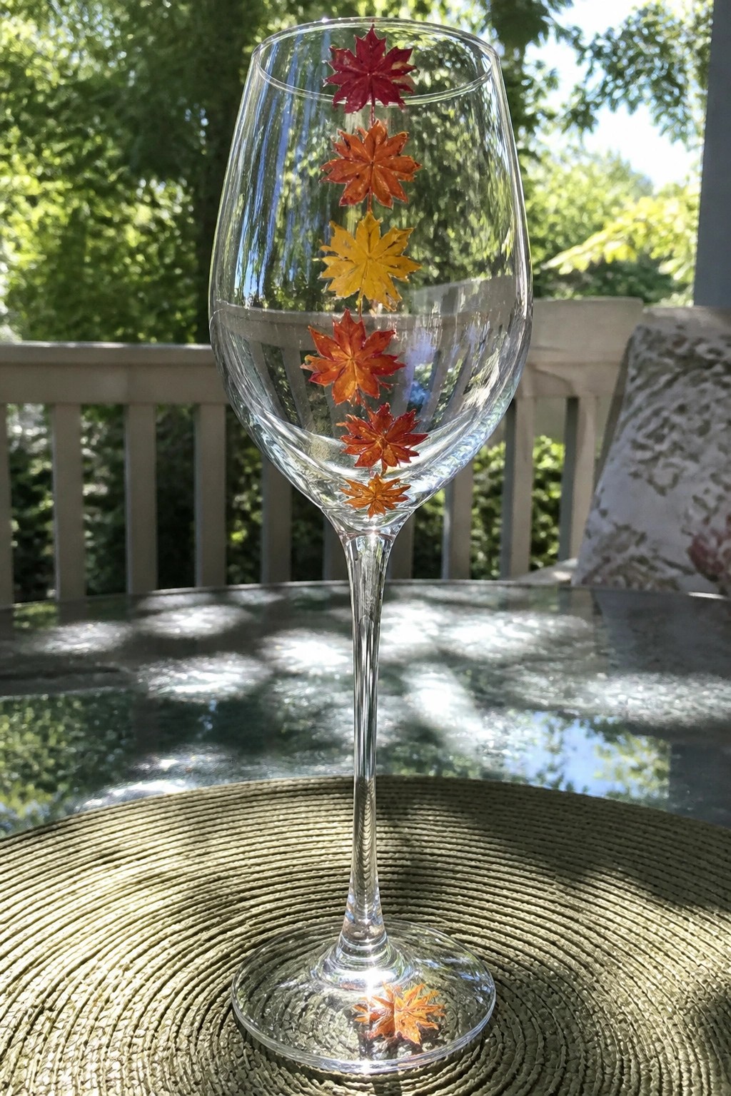 Wine glass with vertical red, orange, and yellow maple leaves on a woven placemat.