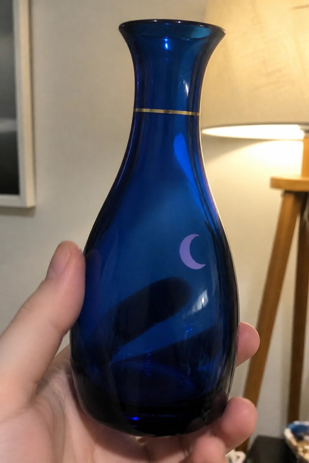 Hand holding deep blue glass vase with gold band and crescent moon