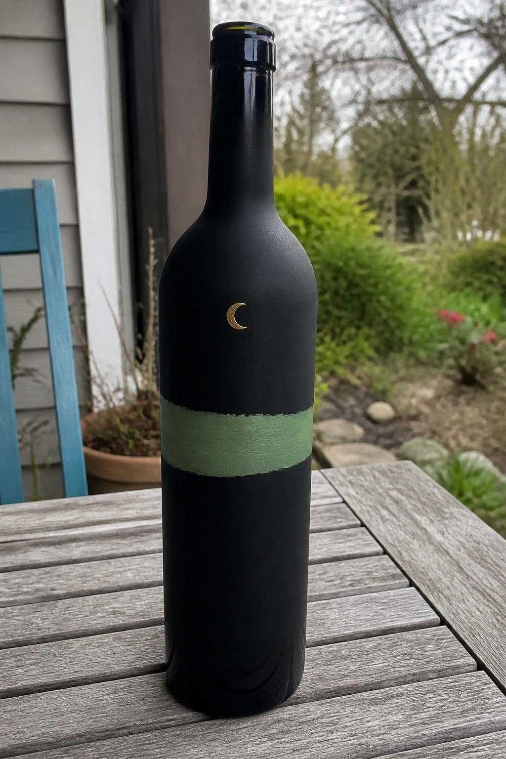 Black wine bottle with green stripe and gold crescent moon on wooden table