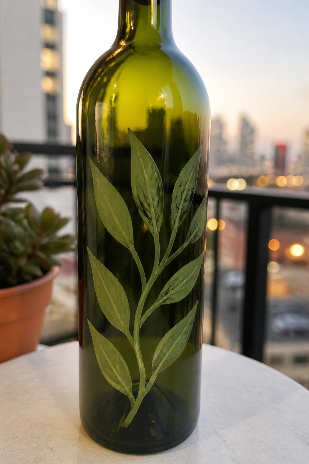 Green glass wine bottle with a painted green leafy branch on a white surface.