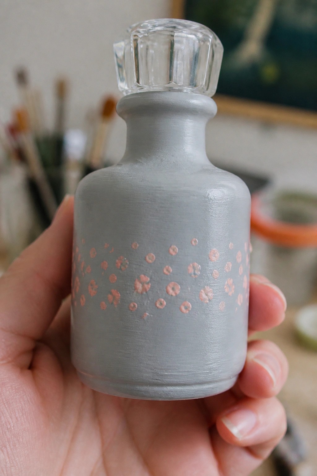 Hand holding gray bottle with rose-gold dots and faceted glass stopper