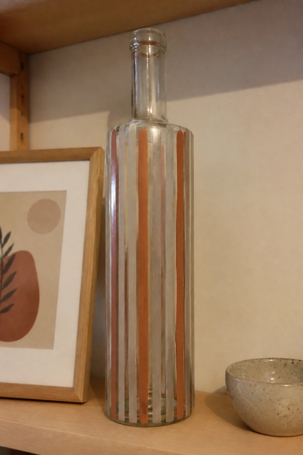Glass bottle with orange and white stripes beside framed art and bowl
