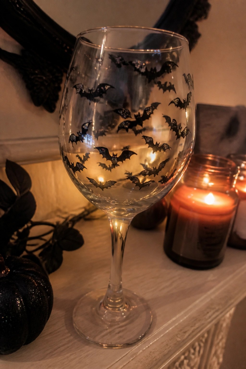 Wine glass with black glitter bats beside lit candle and black pumpkin