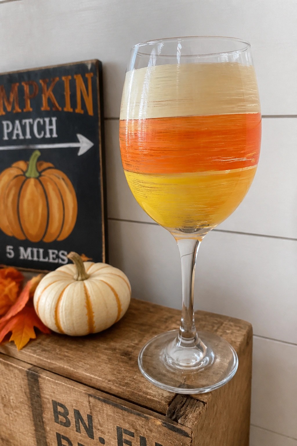 Candy corn striped wine glass on wooden crate with pumpkin patch sign and gourd