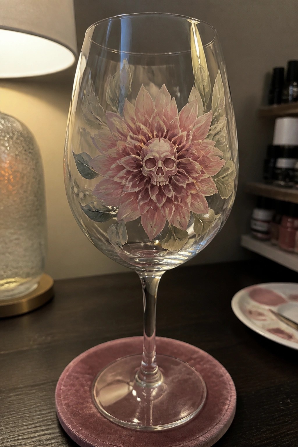Wine glass painted with pink dahlia flower and central skull on pink coaster.