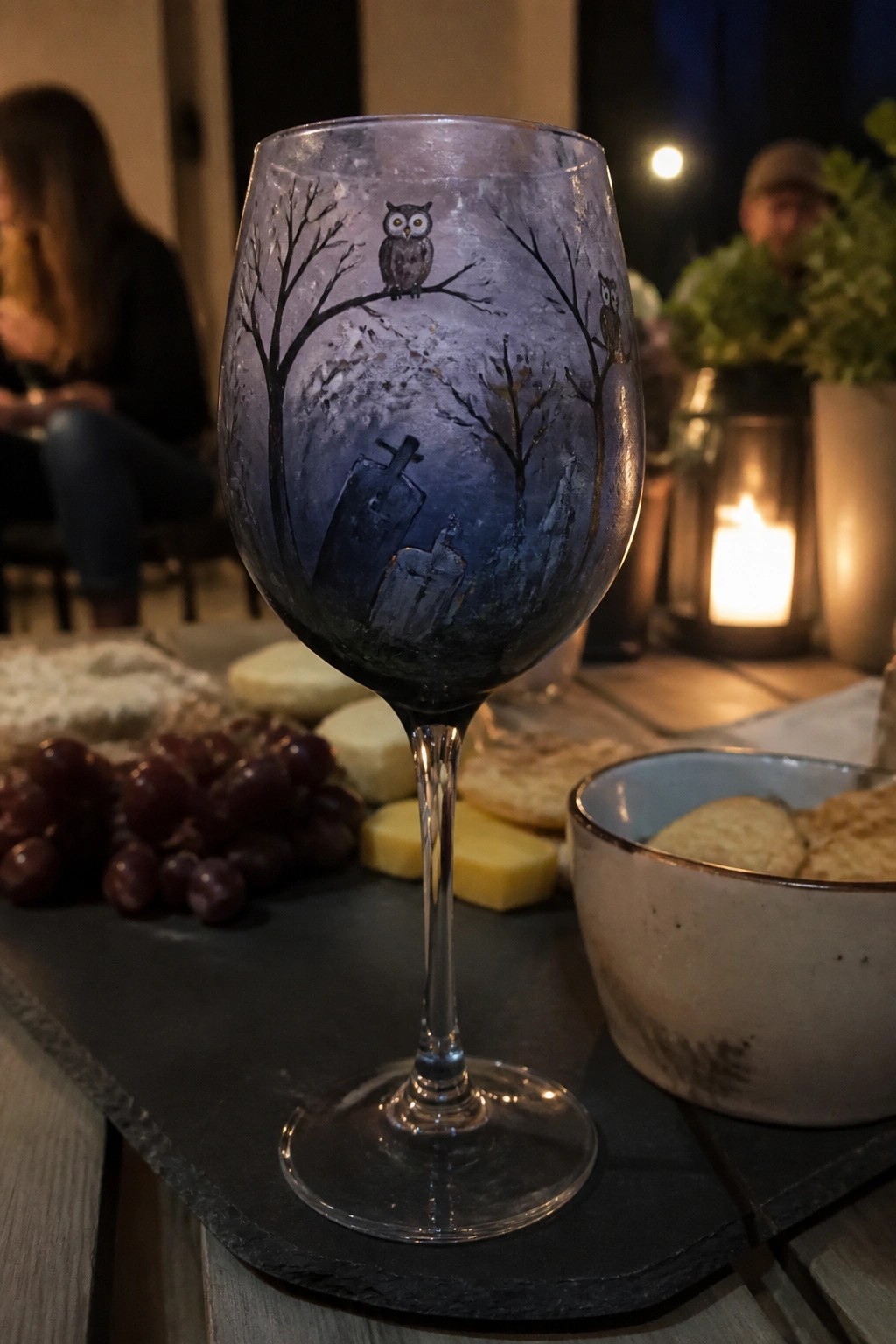 Painted wine glass showing owls on branches above a graveyard with tombstones.