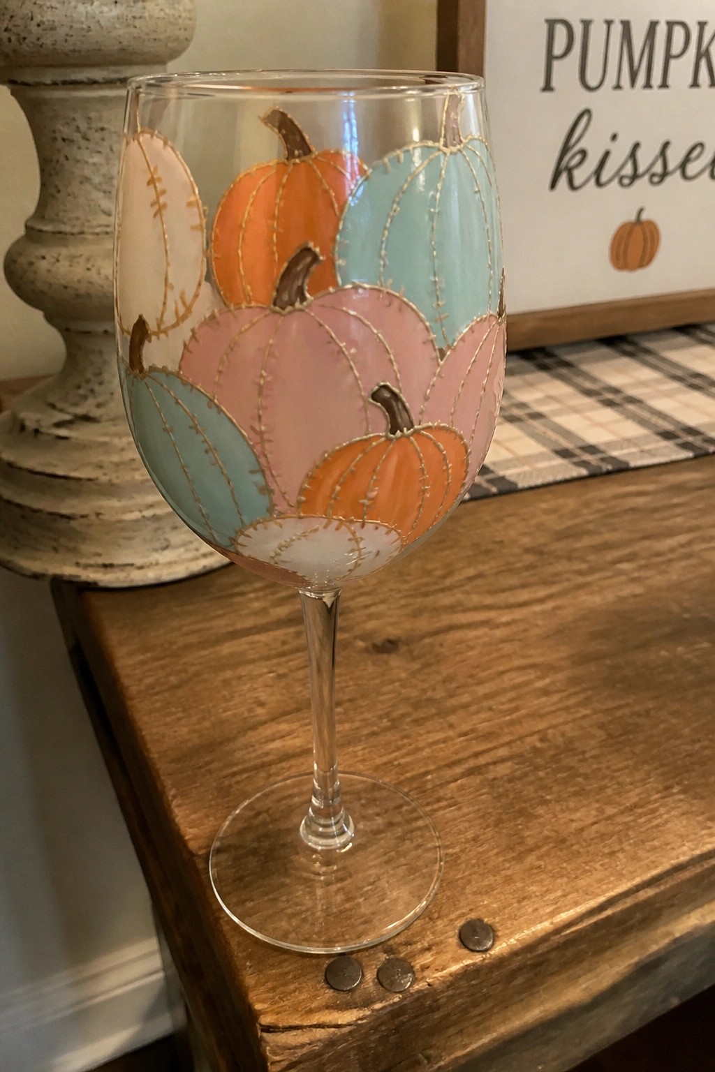 Wine glass painted with colorful stitched pumpkins in orange, pink, and blue on wood
