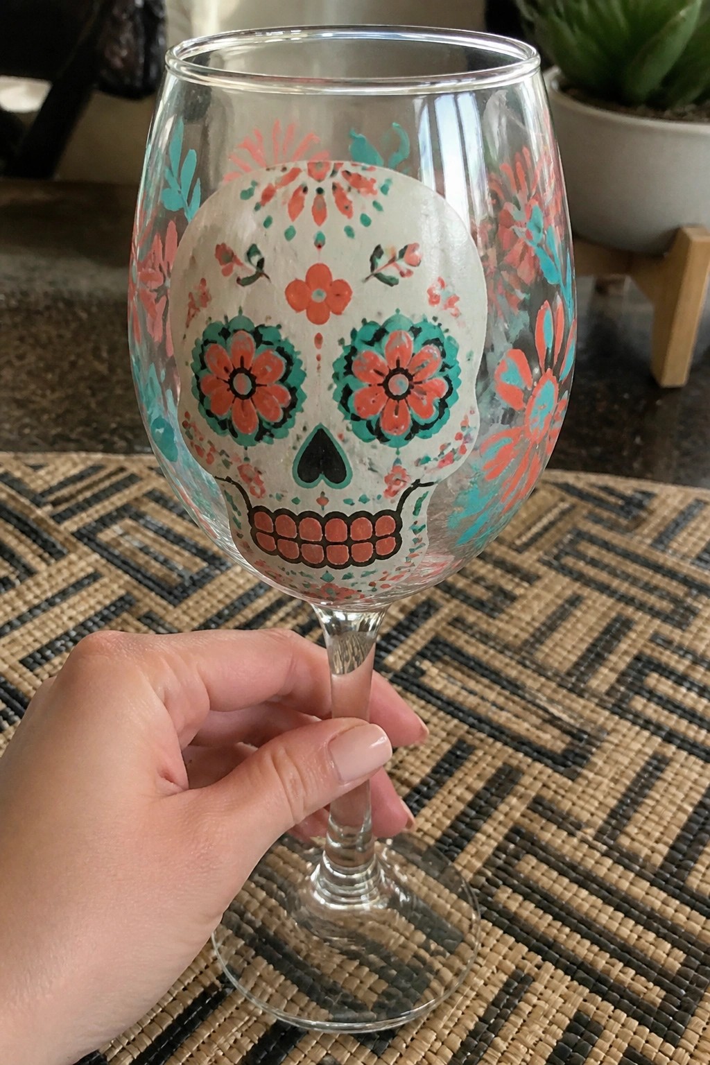 Hand holding wine glass with colorful sugar skull and floral designs on woven mat