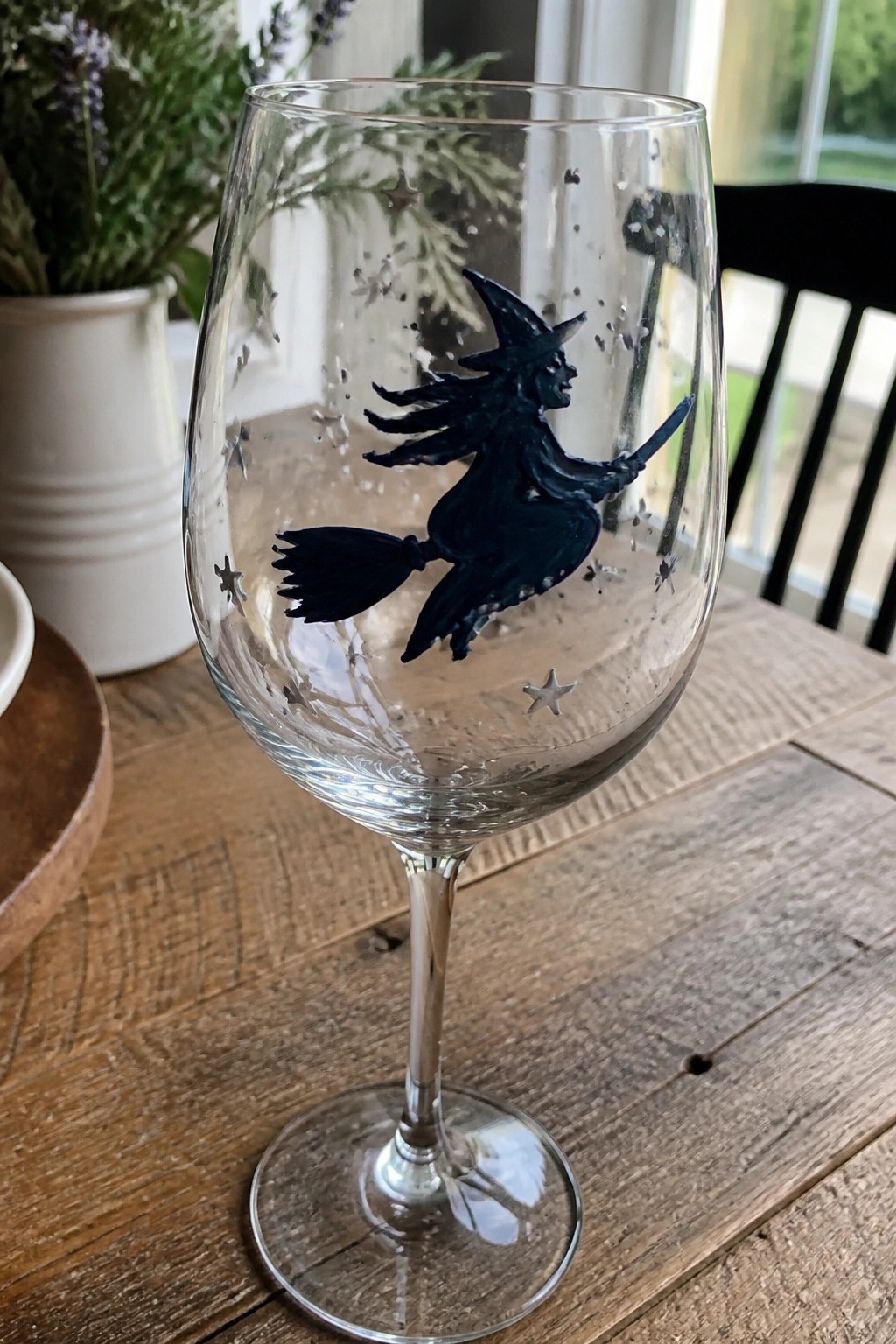 Wine glass with black flying witch on broomstick and scattered stars on wooden table