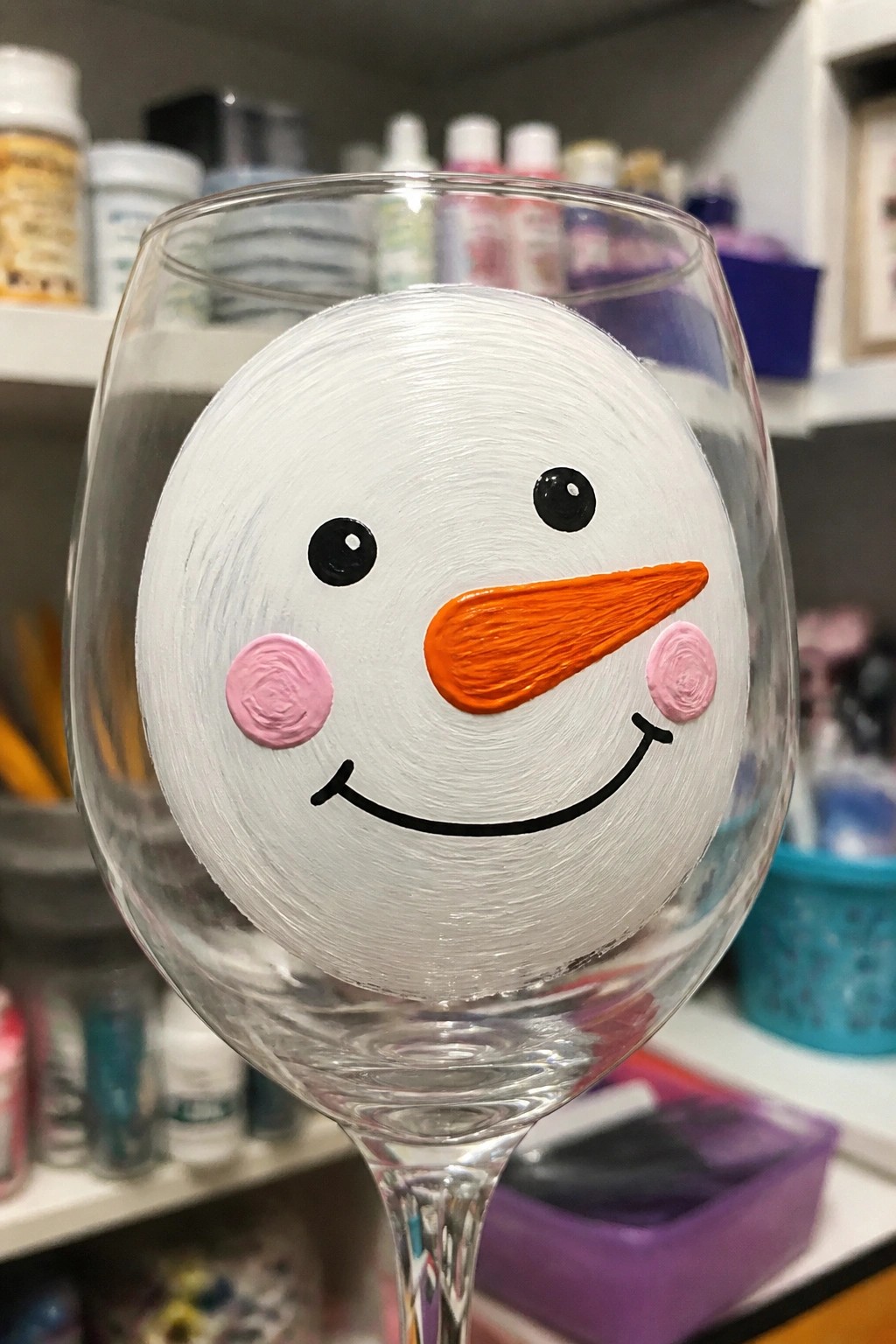 Wine glass with painted snowman face, black eyes, orange nose, and pink cheeks