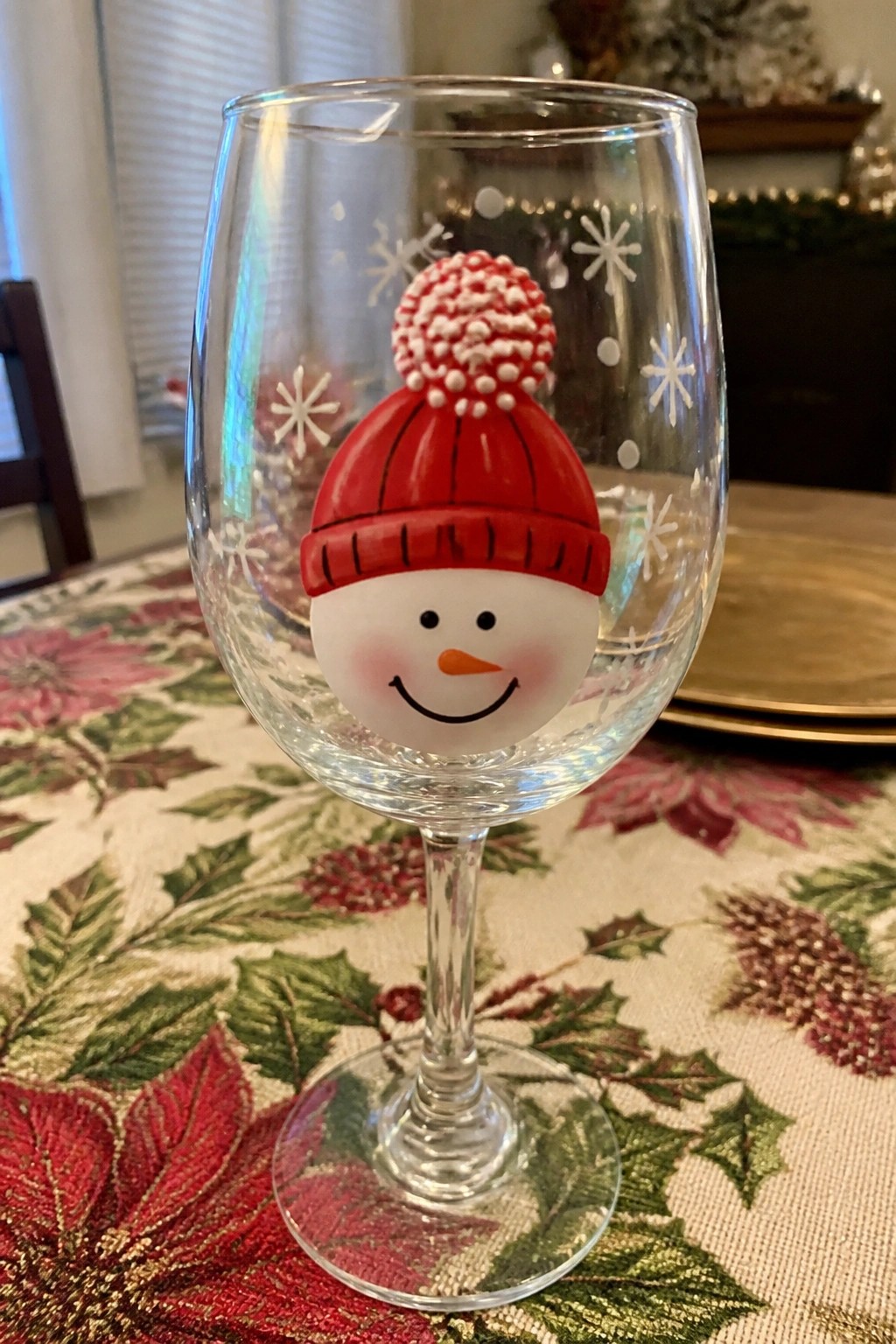 Clear wine glass with snowman face in red pom-pom hat on festive tablecloth