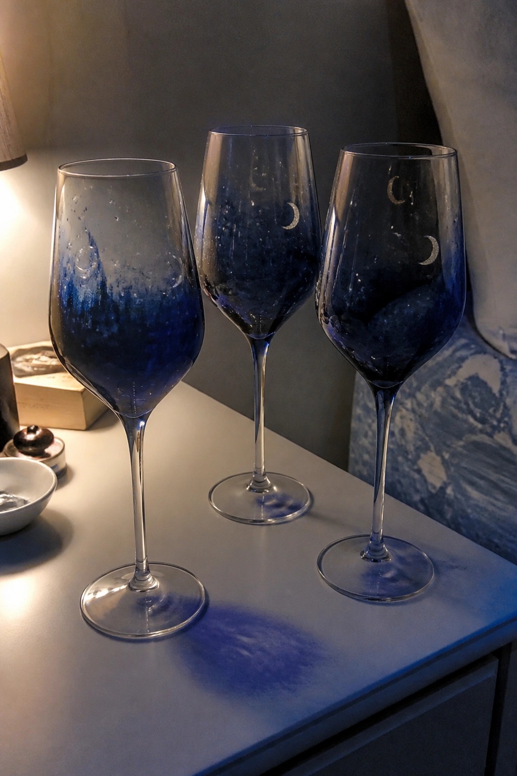 Three blue ombre wine glasses with crescent moons on a bedside table
