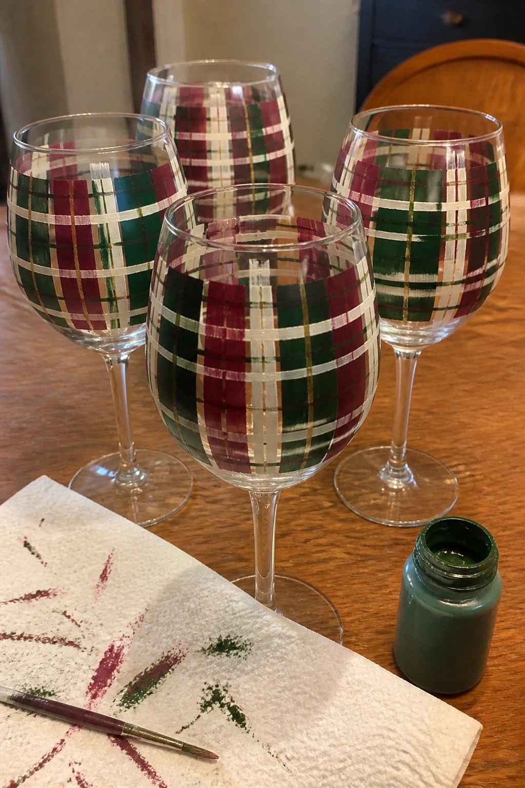 Four plaid wine glasses on wooden table with green paint jar and brush