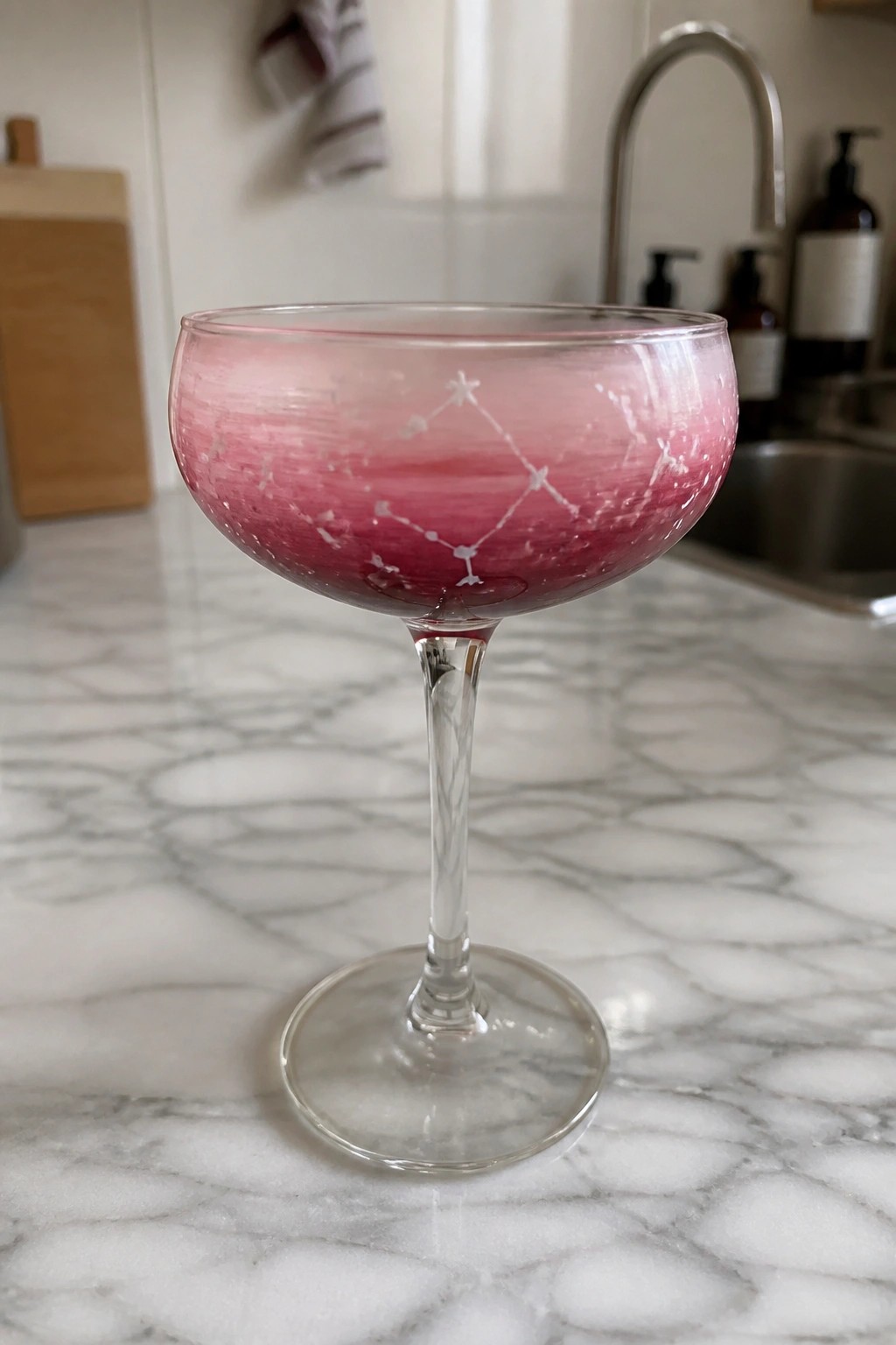 Pink marbled coupe glass with constellation etching on white marble countertop