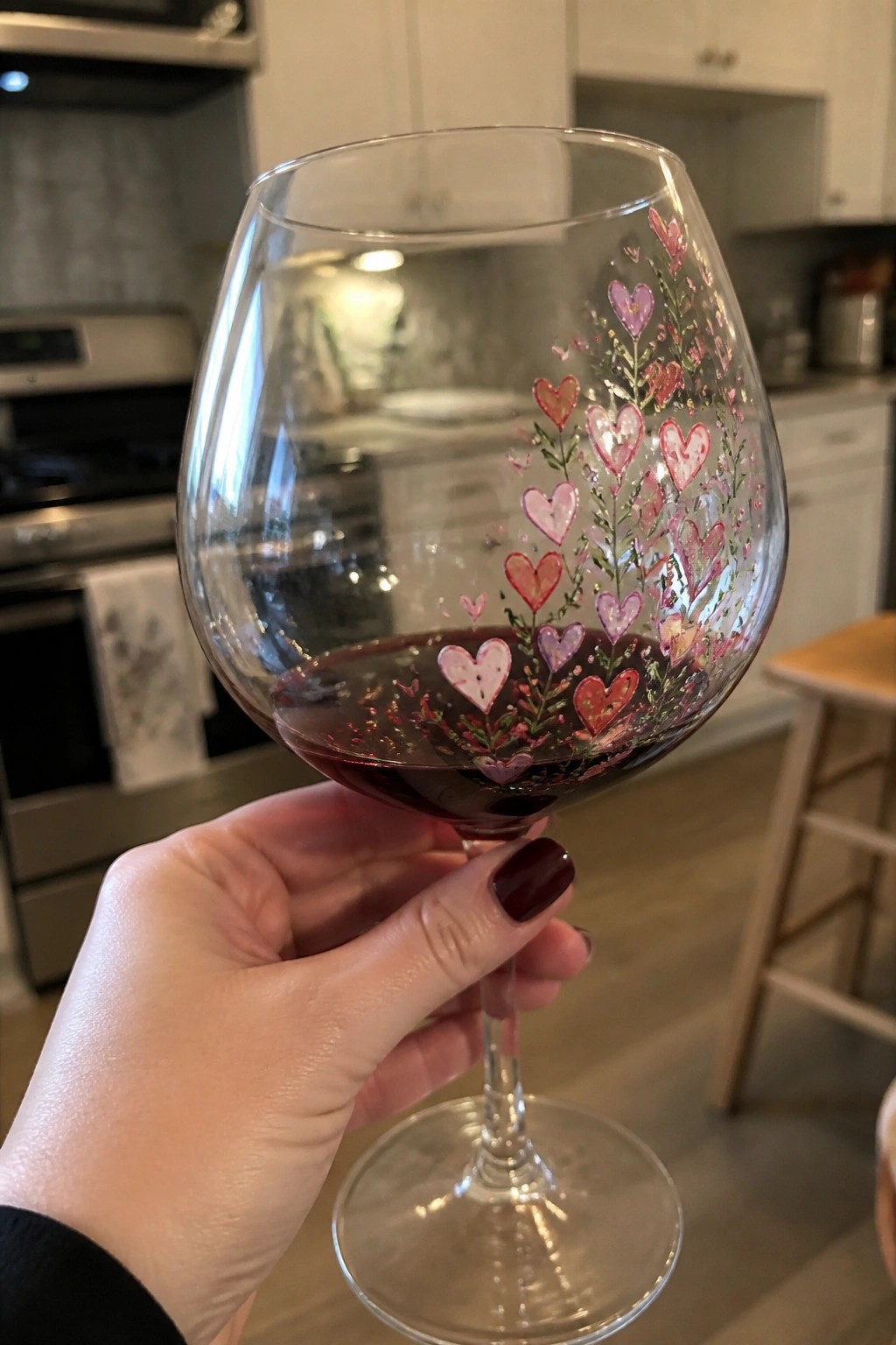 Hand with dark red nails holding wine glass painted with pink hearts