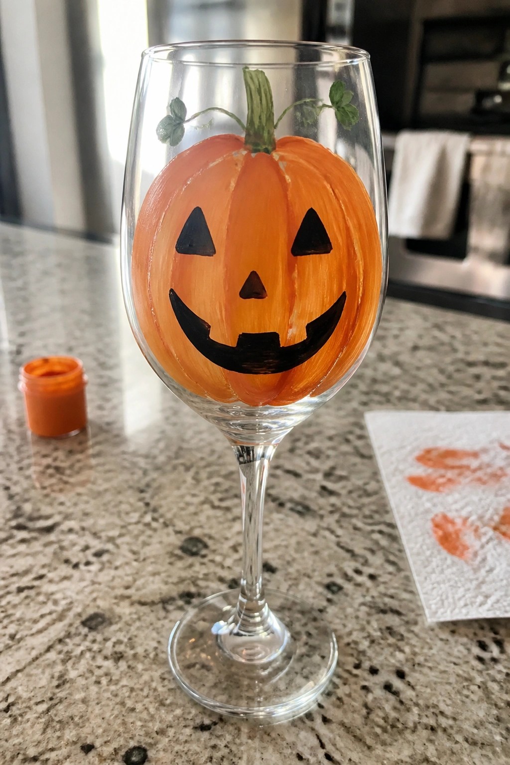 Wine glass hand-painted as orange jack-o'-lantern with black face on marble counter