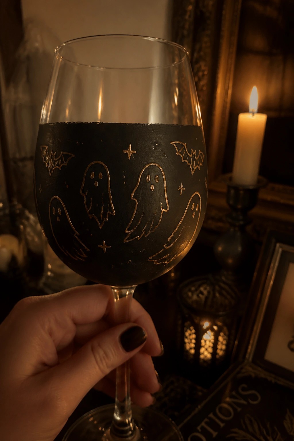 Hand holding black wine glass with gold ghosts, bats, and stars by candlelight