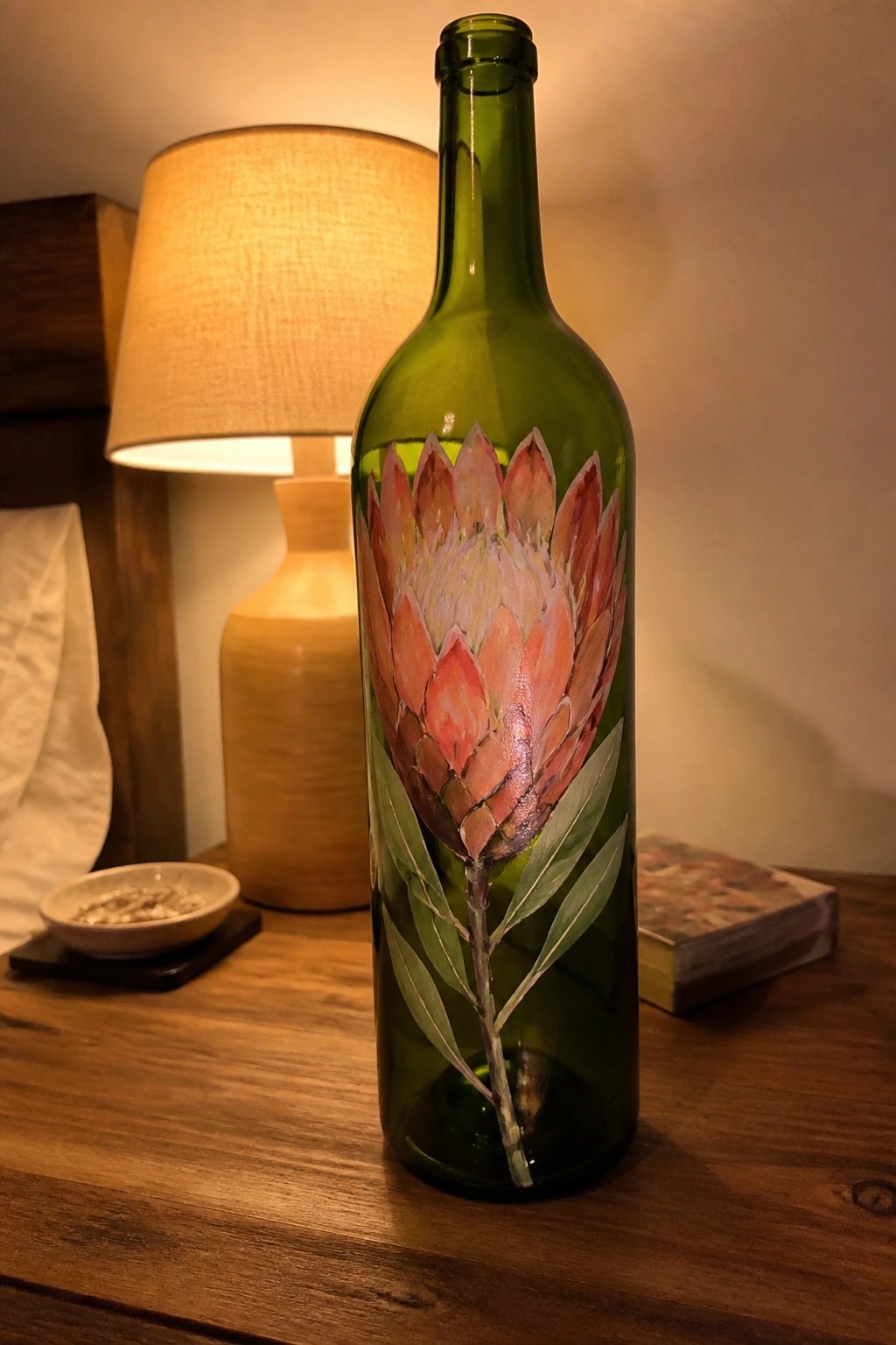 Green glass bottle hand-painted with pink protea flower on wooden table