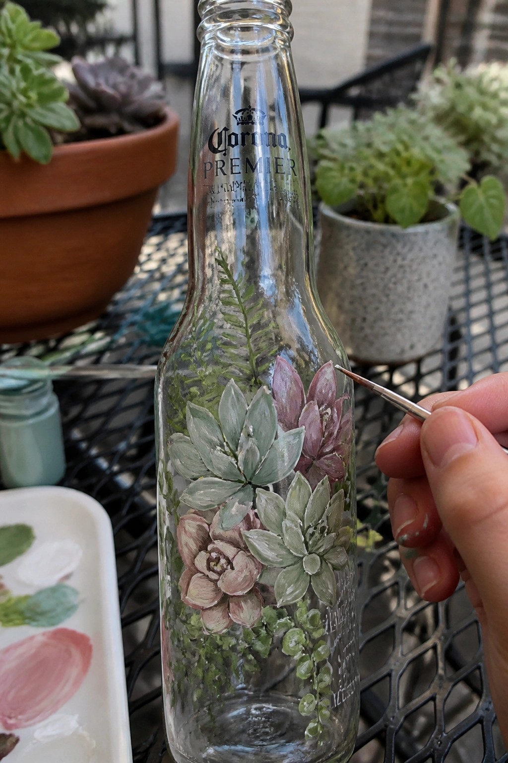 Hand painting pink and green succulents on a clear Corona Premier bottle.