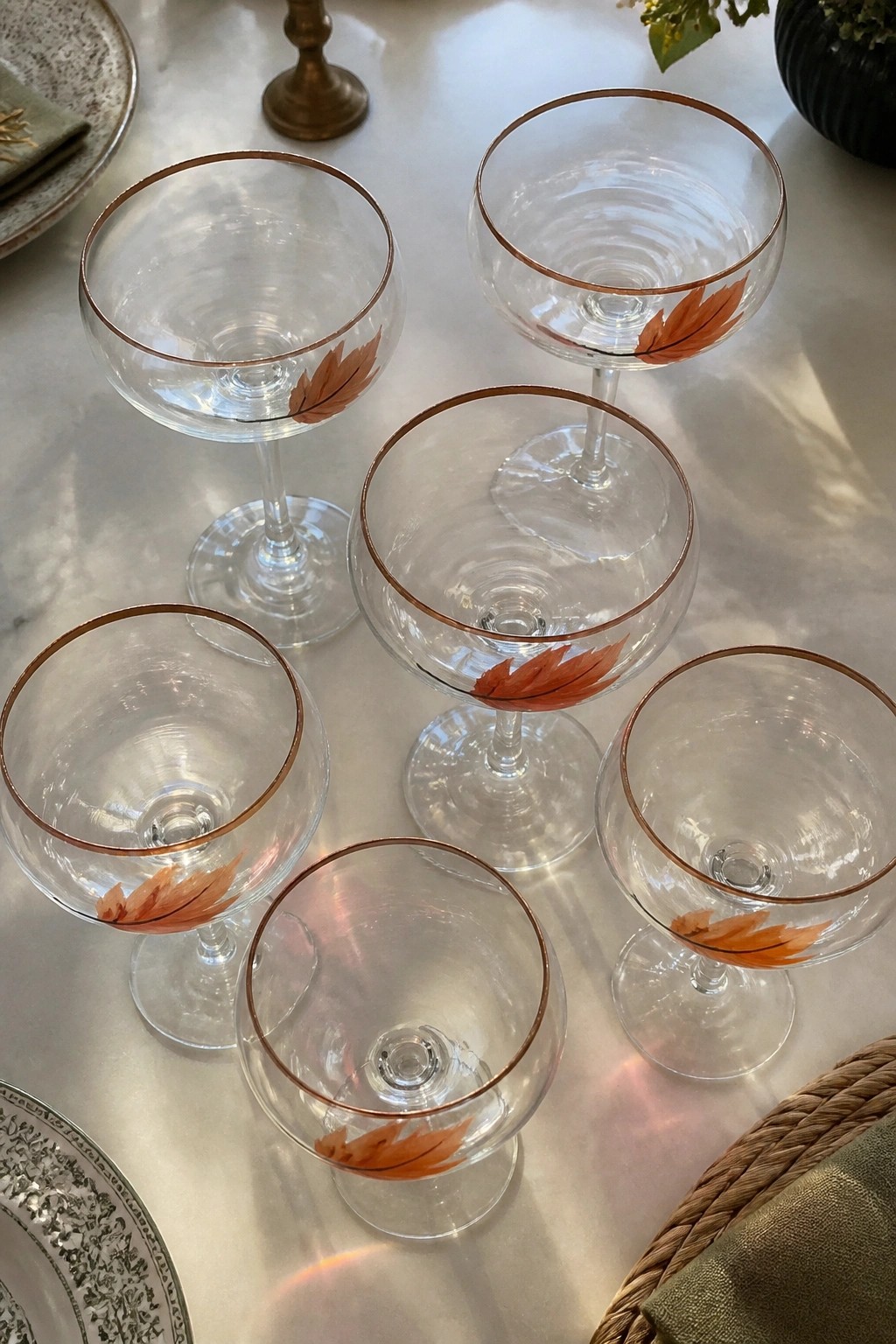 Six coupe glasses with gold rims and orange leaf designs on marble table