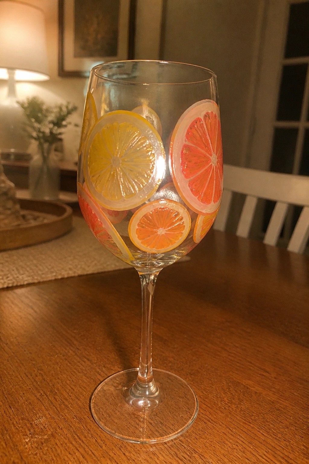 Wine glass painted with colorful lemon, orange, and grapefruit slices on wooden table