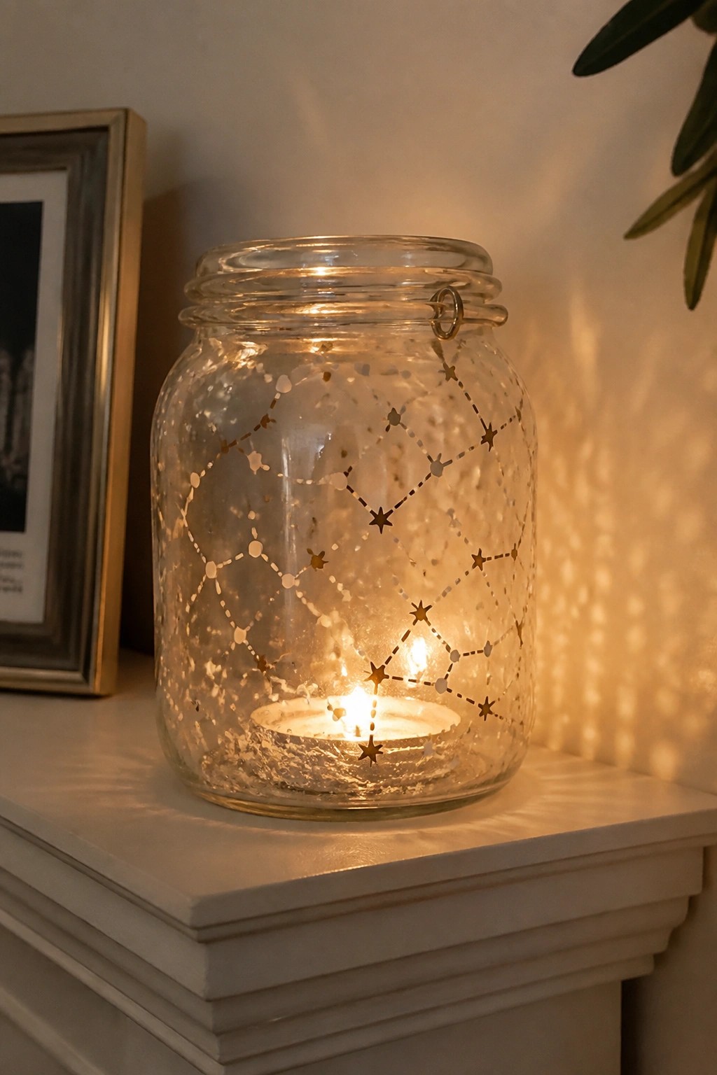 Lit glass jar with star cutouts and candle on white mantel beside frame