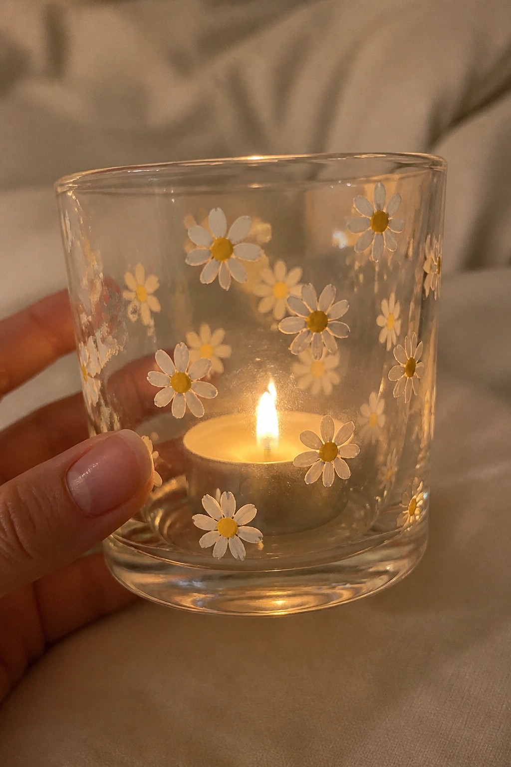Hand holding glass votive with daisy designs and lit tea light candle