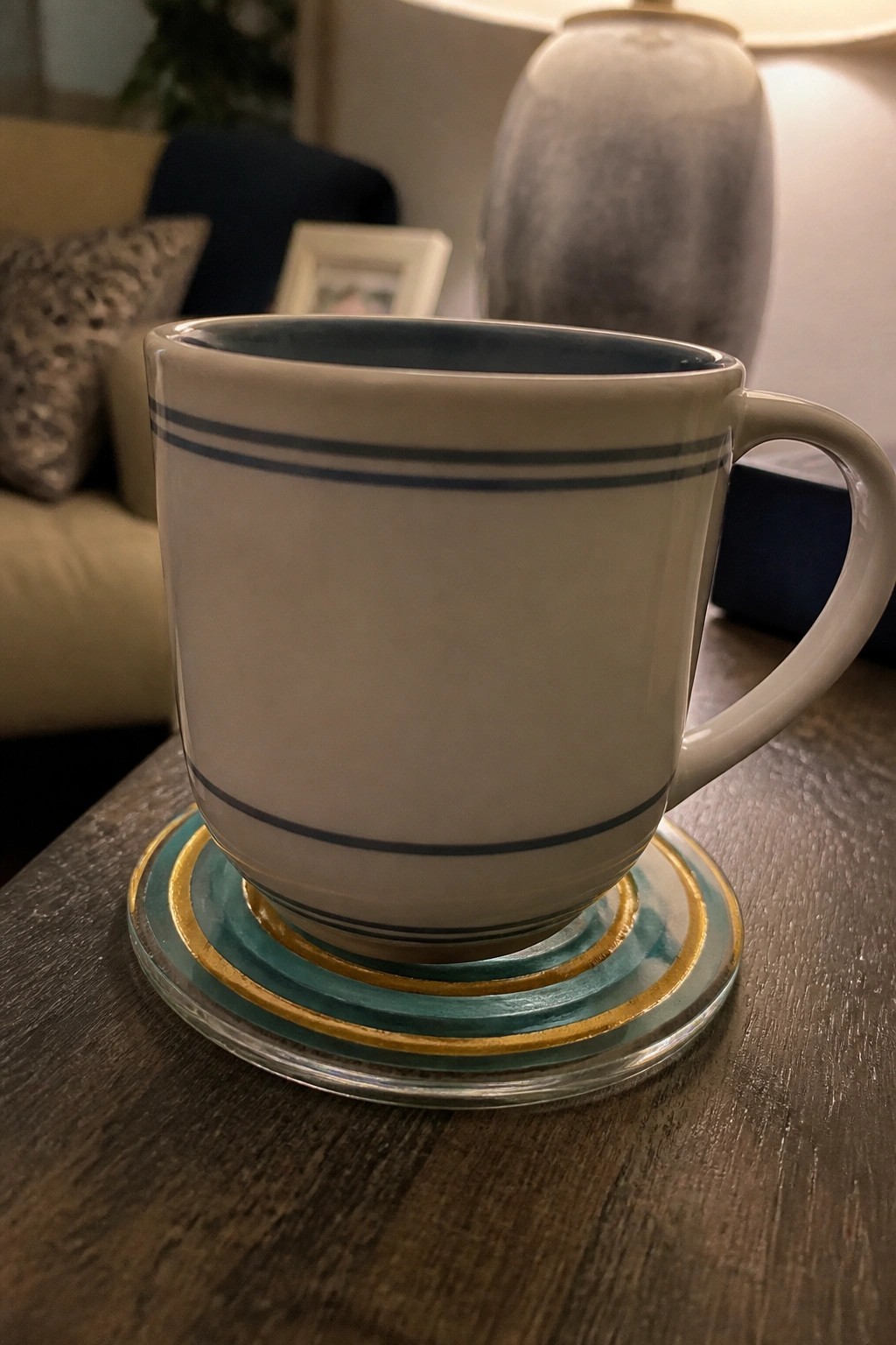 White mug with blue stripes on teal and gold coaster atop wooden table