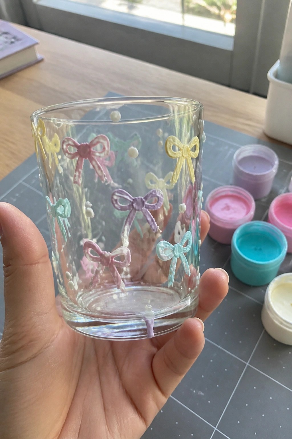 Hand holding clear glass cup decorated with colorful pastel bow designs and dots