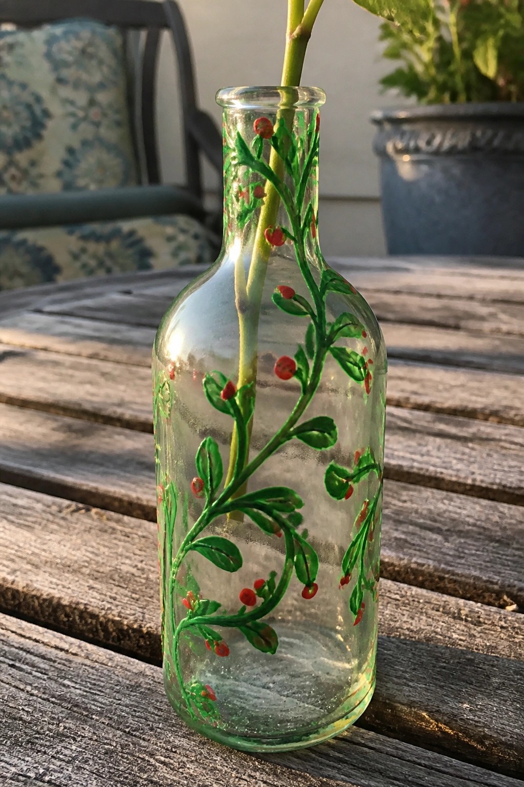 Clear glass bottle with green vines and red berries holding a plant stem on wooden table