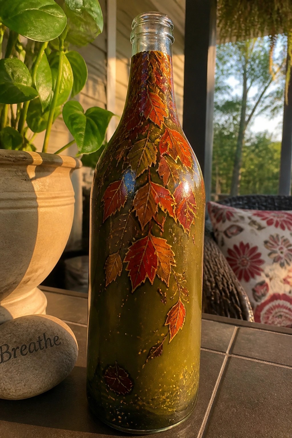 Glass bottle painted with red and orange autumn leaves on patio table