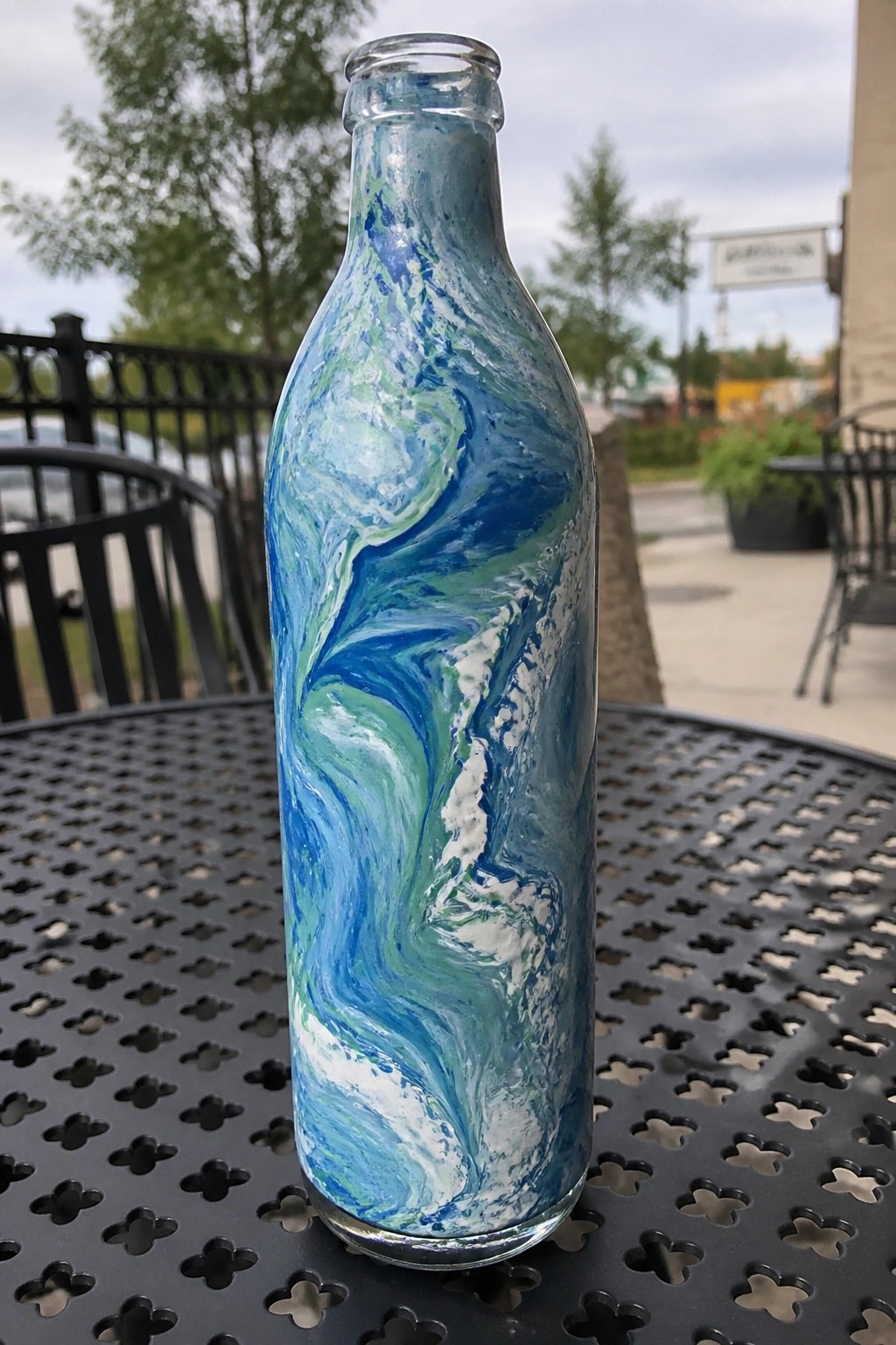 Painted glass bottle with swirling blue green white patterns on black metal table