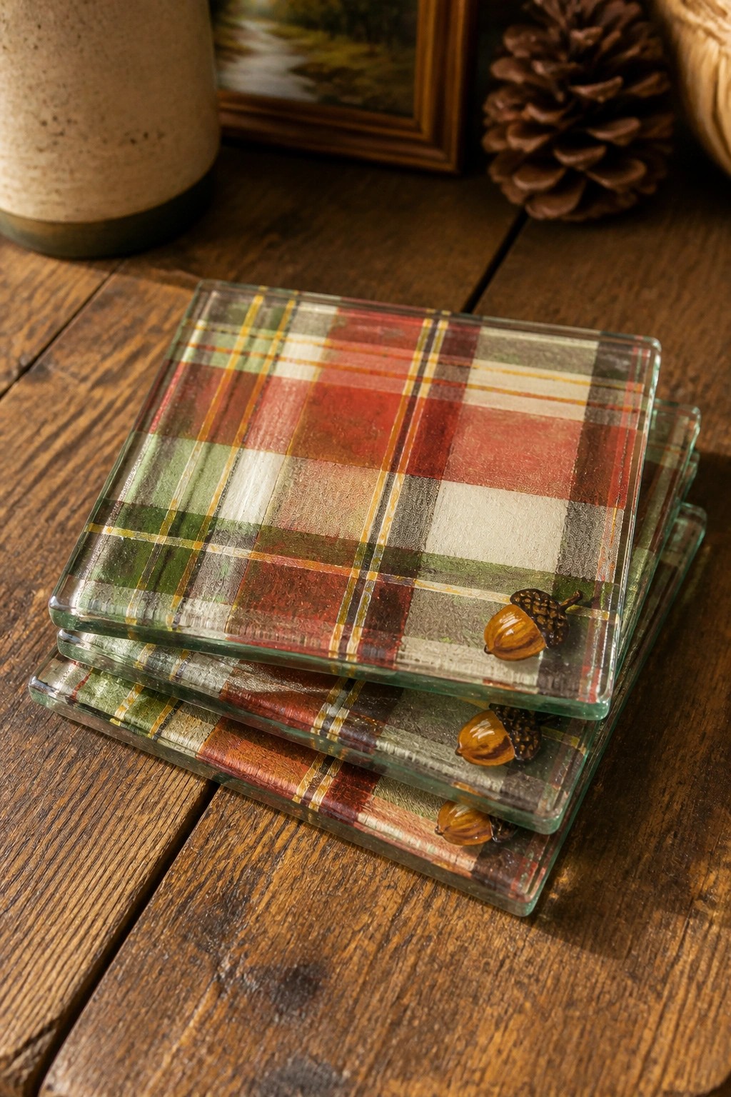 Stacked plaid glass coasters with acorn accents on wooden table