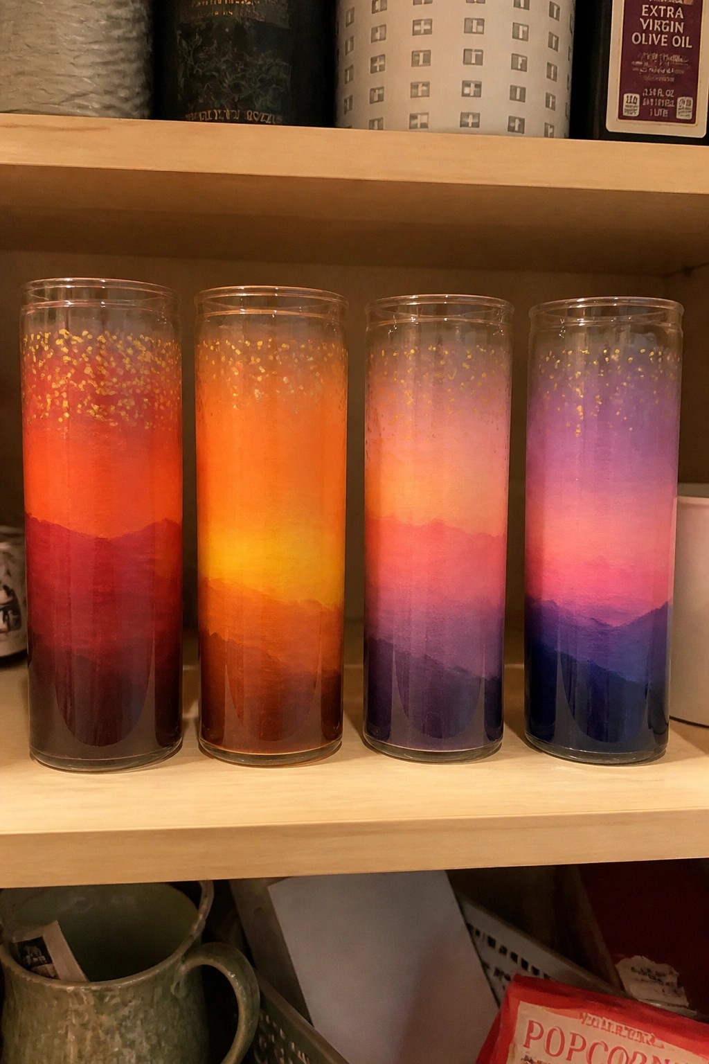 Four gradient candles with mountain silhouettes and gold glitter on a wooden shelf.