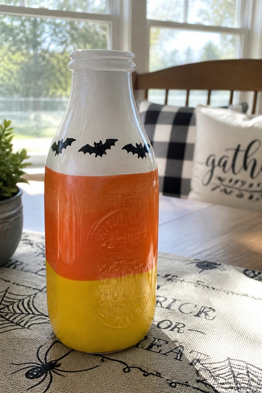 Candy corn painted bottle with black bats on spiderweb Halloween tablecloth