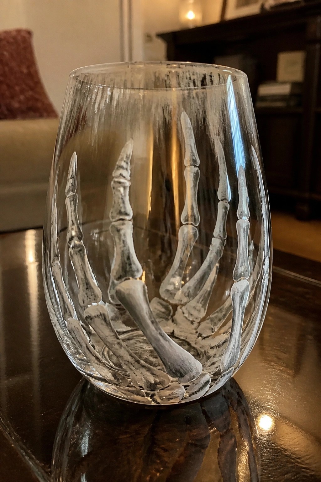 Clear glass tumbler etched with white skeletal hands on dark wooden table.