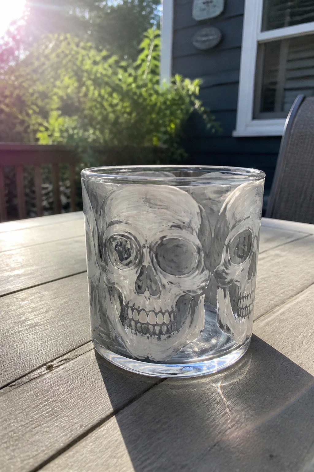 Clear glass tumbler with skull designs on sunlit wooden outdoor table