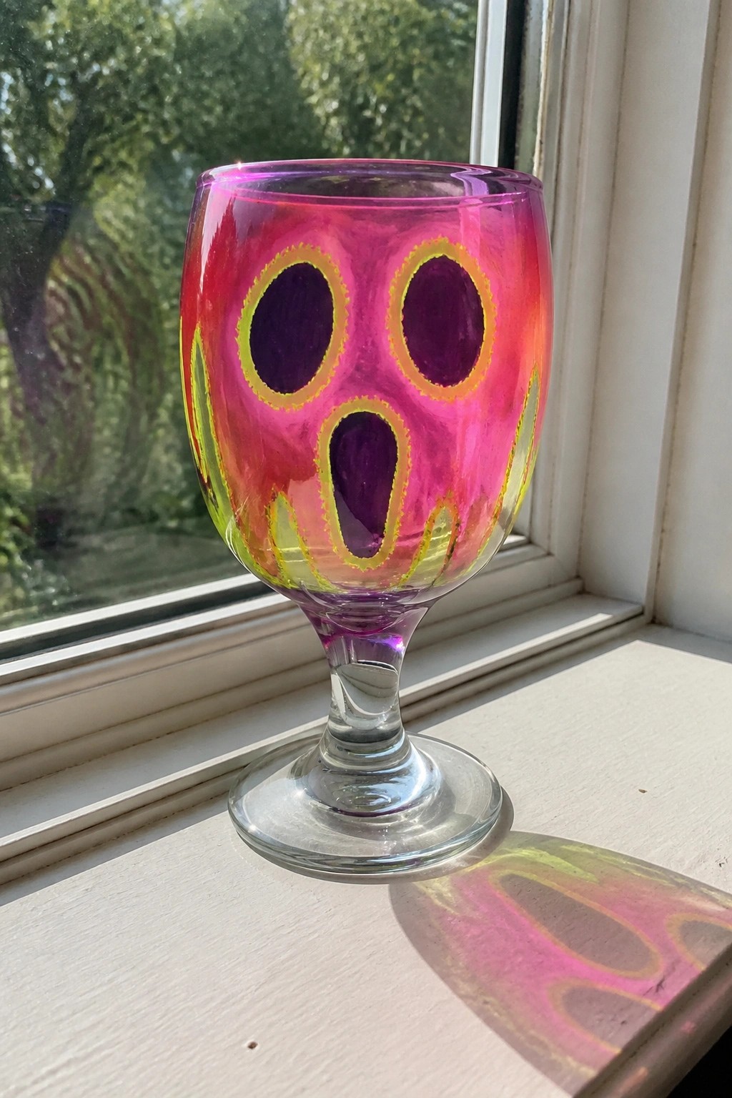 Brightly painted pink glass goblet with purple face on sunny windowsill