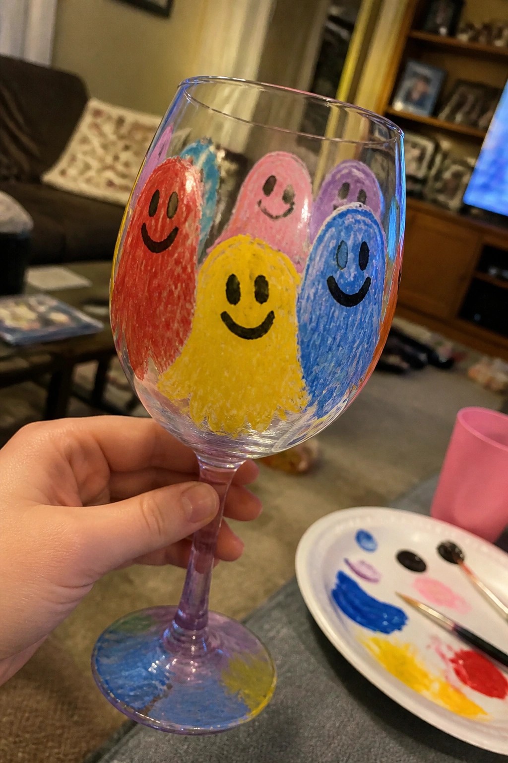 Hand holding wine glass painted with red, yellow, blue, pink smiley faces